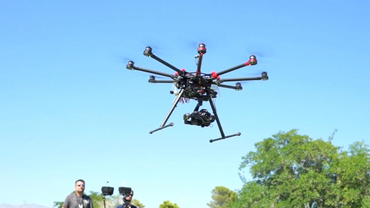 Camera drone in flight over a park with the pilot below